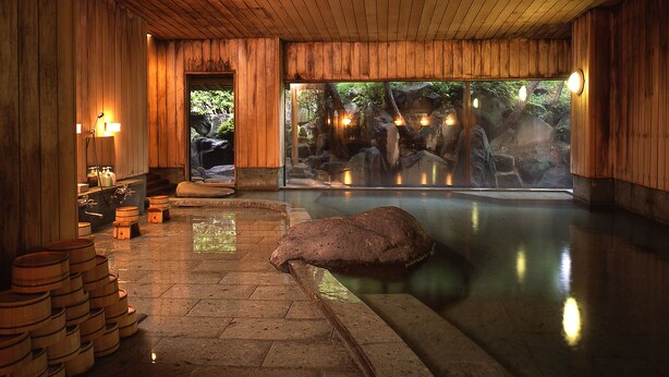 A wooden interior with a stone pool, wooden barrels, and a view of a natural landscape. - Nunohan (Suwa)