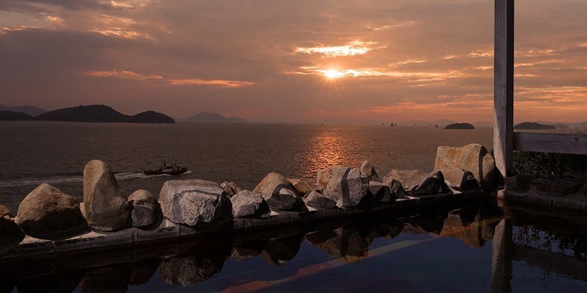 A sunset over water with rocks and a pier.