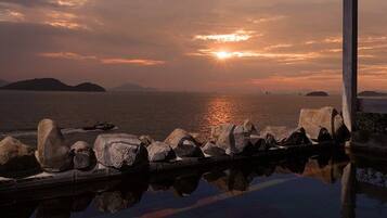 A sunset over water with rocks and a pier.