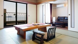 A traditional Japanese room with tatami flooring, a low table with a cushion, a sofa, and a sliding door leading to a balcony with a view. - Washu Onsen Bizenya Koushi (Kurashiki)