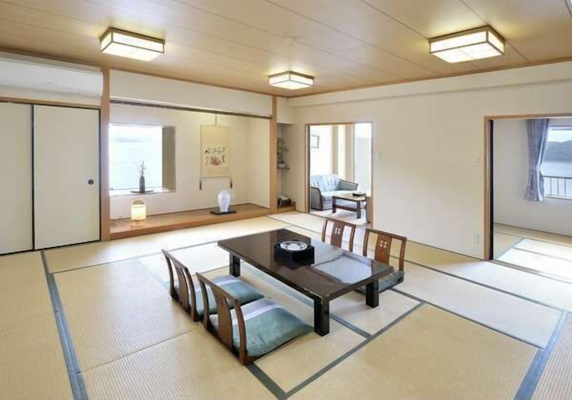 Une pièce avec un sol recouvert de tatamis, une petite table et des bancs, une porte coulissante et une vue sur l’extérieur.