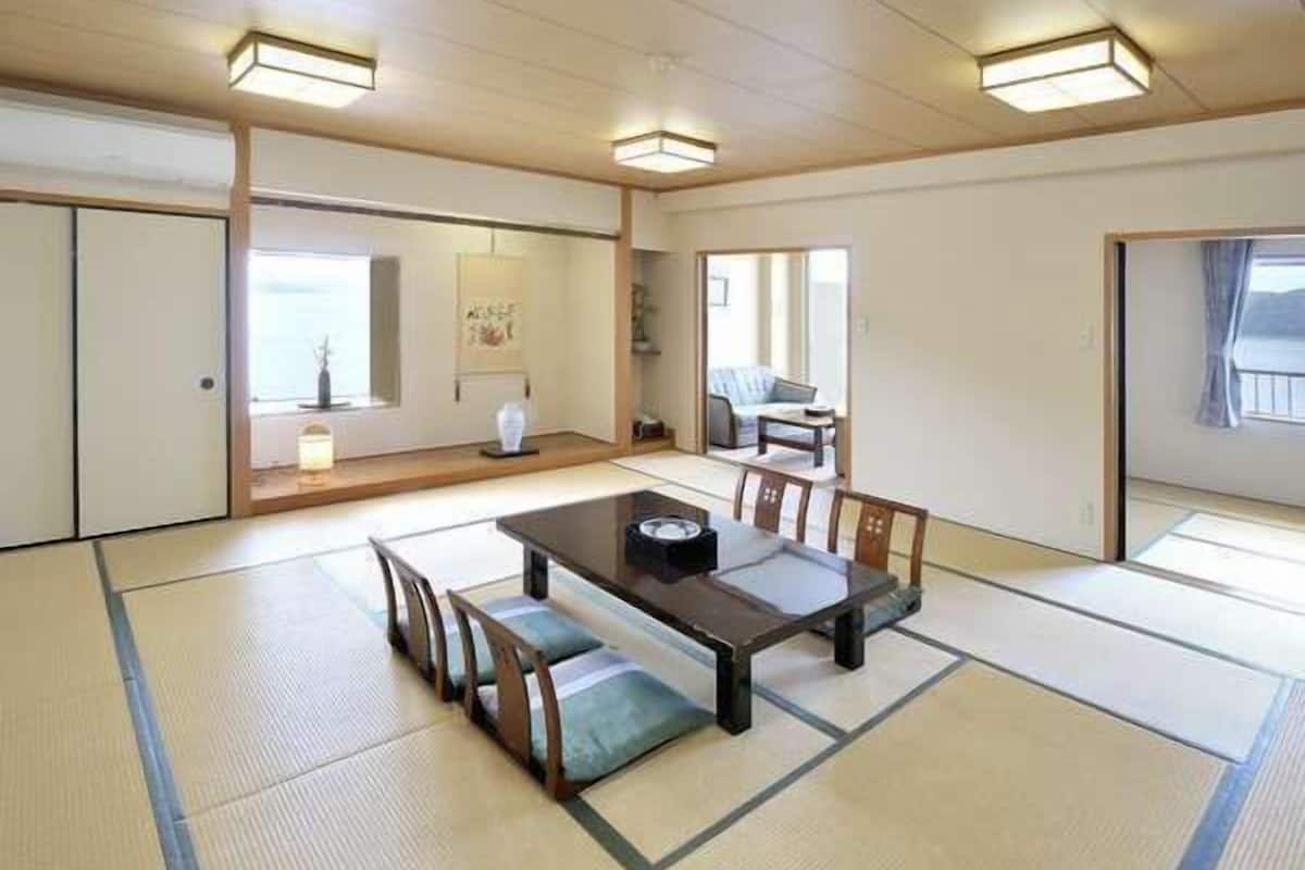 Una habitación con tatami, una mesa baja, bancos, una puerta corredera y vistas al exterior.