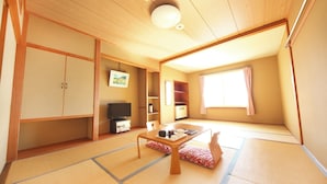 Una habitación japonesa tradicional con suelo de tatami, televisión, armario y ventana con cortinas.