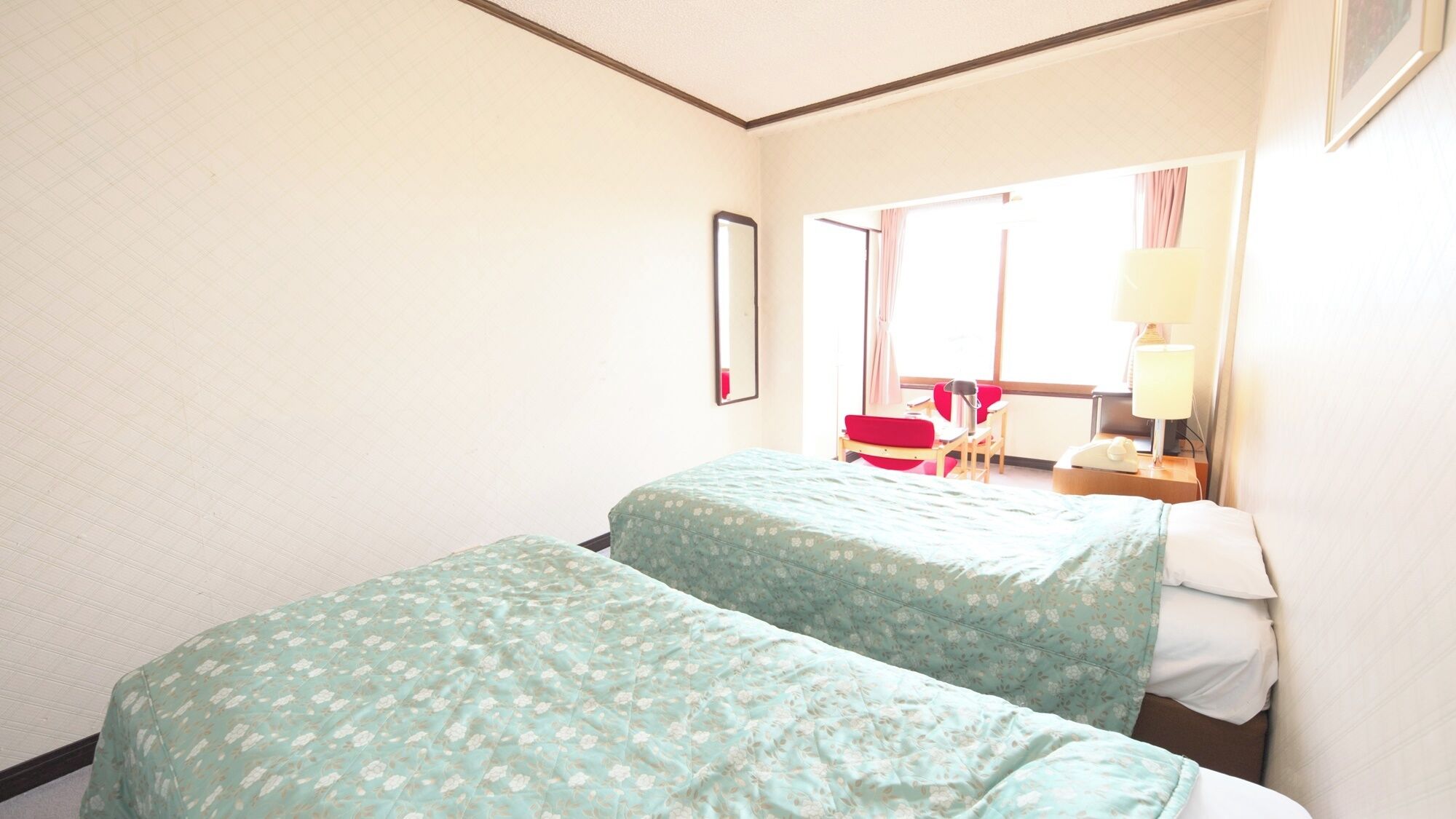 Hotellihuone, jossa on kaksi sänkyä, peili, työpöytä tuolilla sekä ikkuna, jossa on verhot.