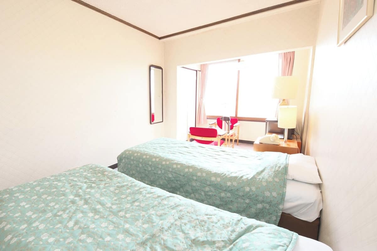 Hotellihuone, jossa on kaksi sänkyä, peili, työpöytä tuolilla sekä ikkuna, jossa on verhot.