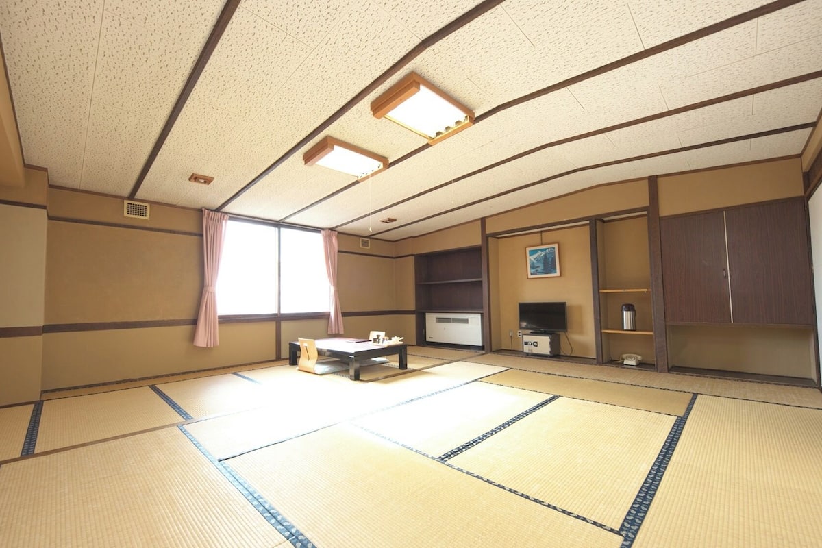 Ein traditioneller Raum mit Tatami-Matten, einem Fernseher, einem kleinen Tisch und einem Schrank.