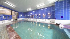 An indoor swimming pool with blue tiled walls and multiple showerheads.
