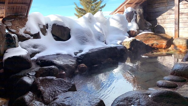 Un área de aguas termales con rocas y agua, rodeada de construcciones de madera.