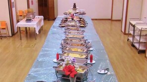 A buffet setup with multiple trays of food, a table with a white tablecloth, and a vase with flowers.