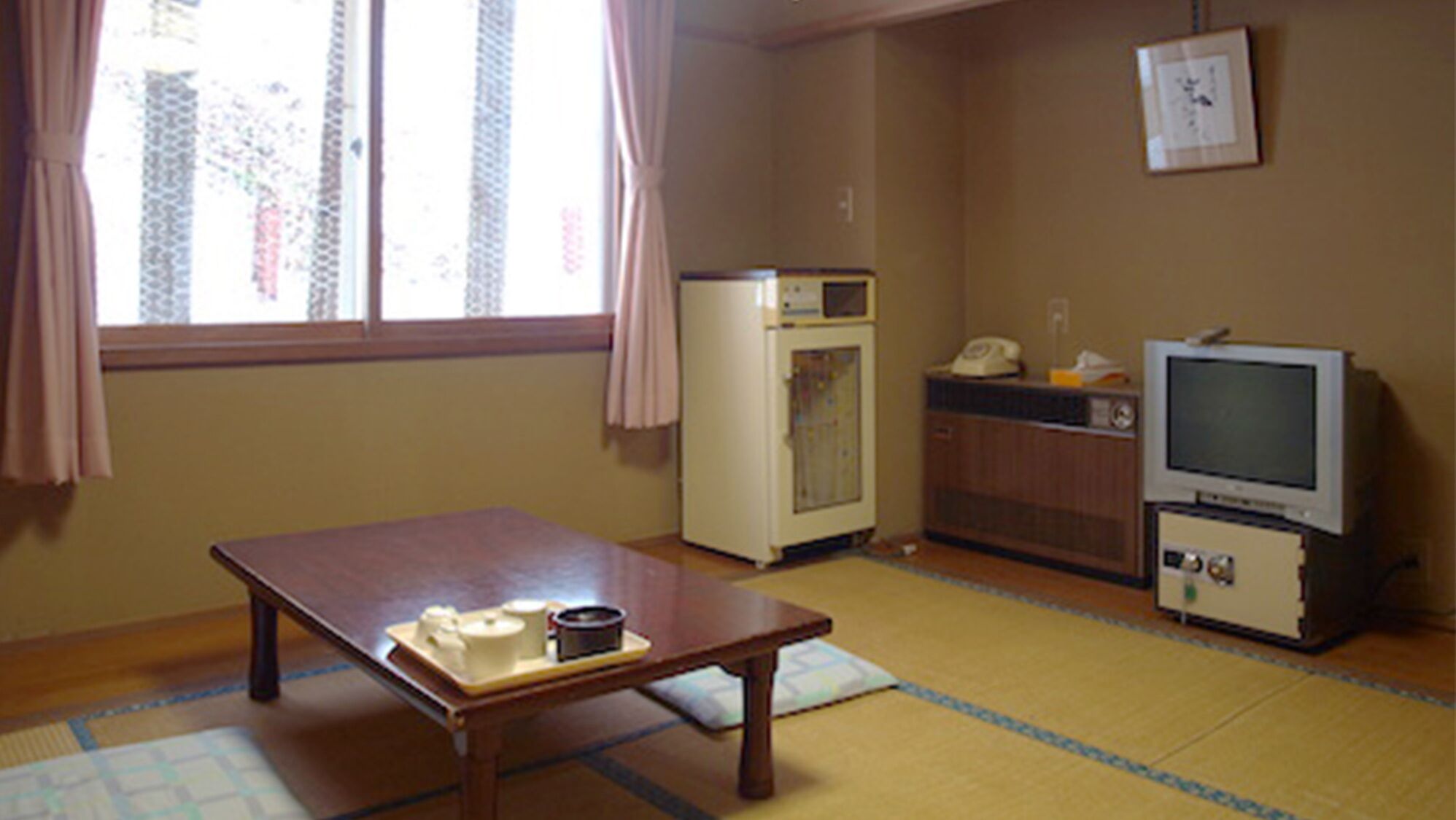 A room with a tatami mat floor, a wooden table with cups and a small container, a refrigerator, a microwave, a telephone, and a television.