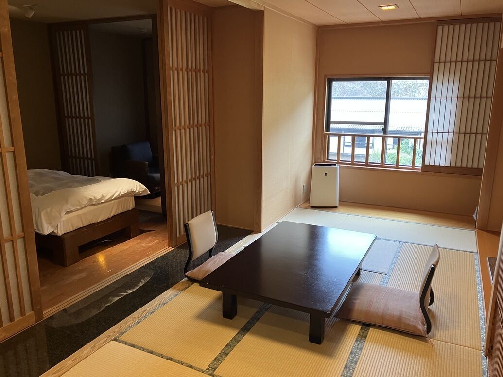 Een traditionele Japanse kamer met tatami vloerbedekking, een lage tafel, een bed en schuifdeuren.