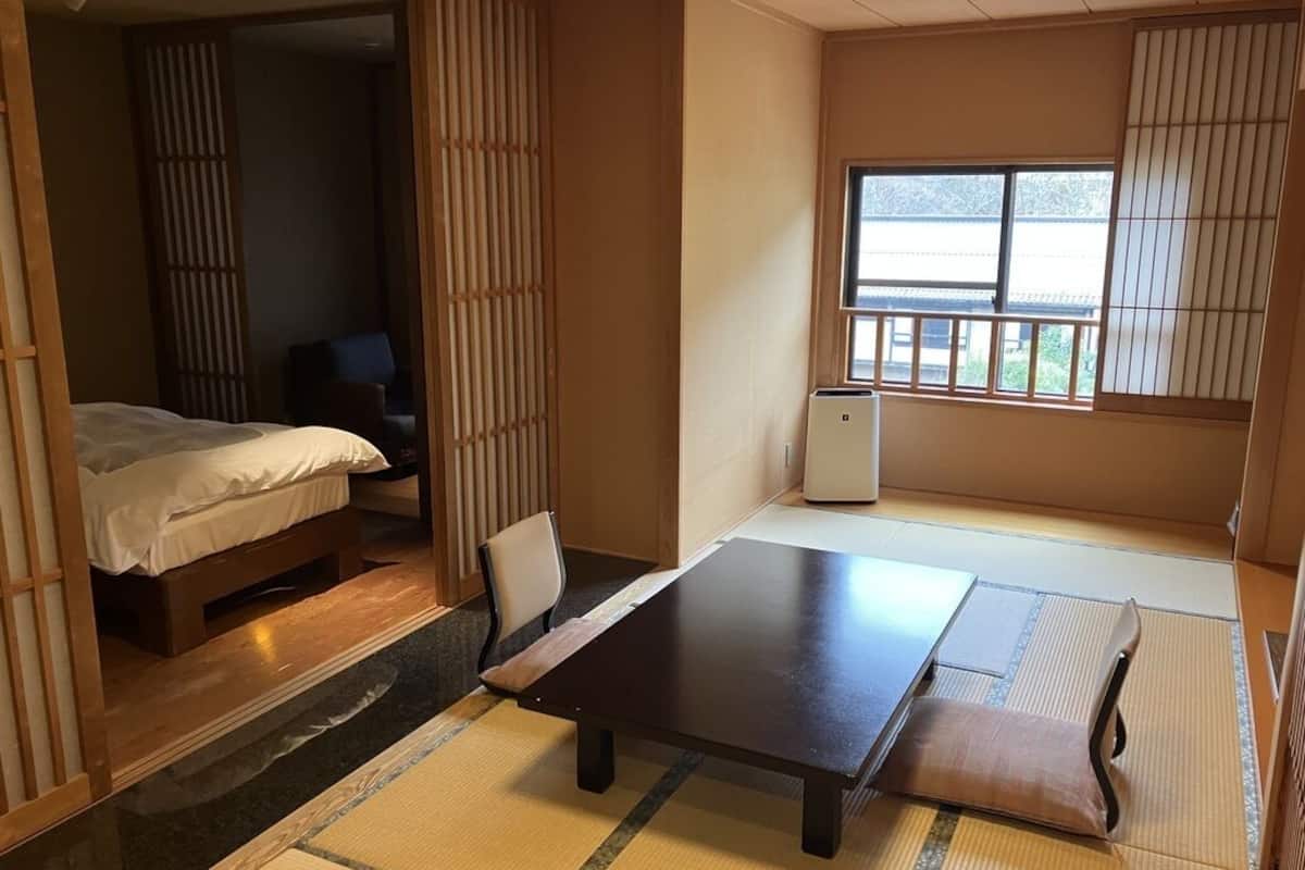 Une pièce de style japonais traditionnel, avec un sol recouvert de tatamis, une table basse, un lit et des portes coulissantes.