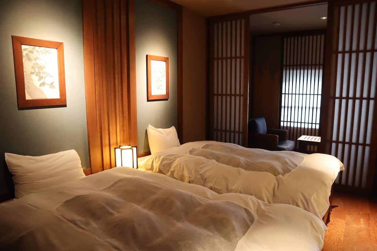 Une chambre d’hôtel avec deux lits, un bureau et une vue à travers un paravent en papier.
