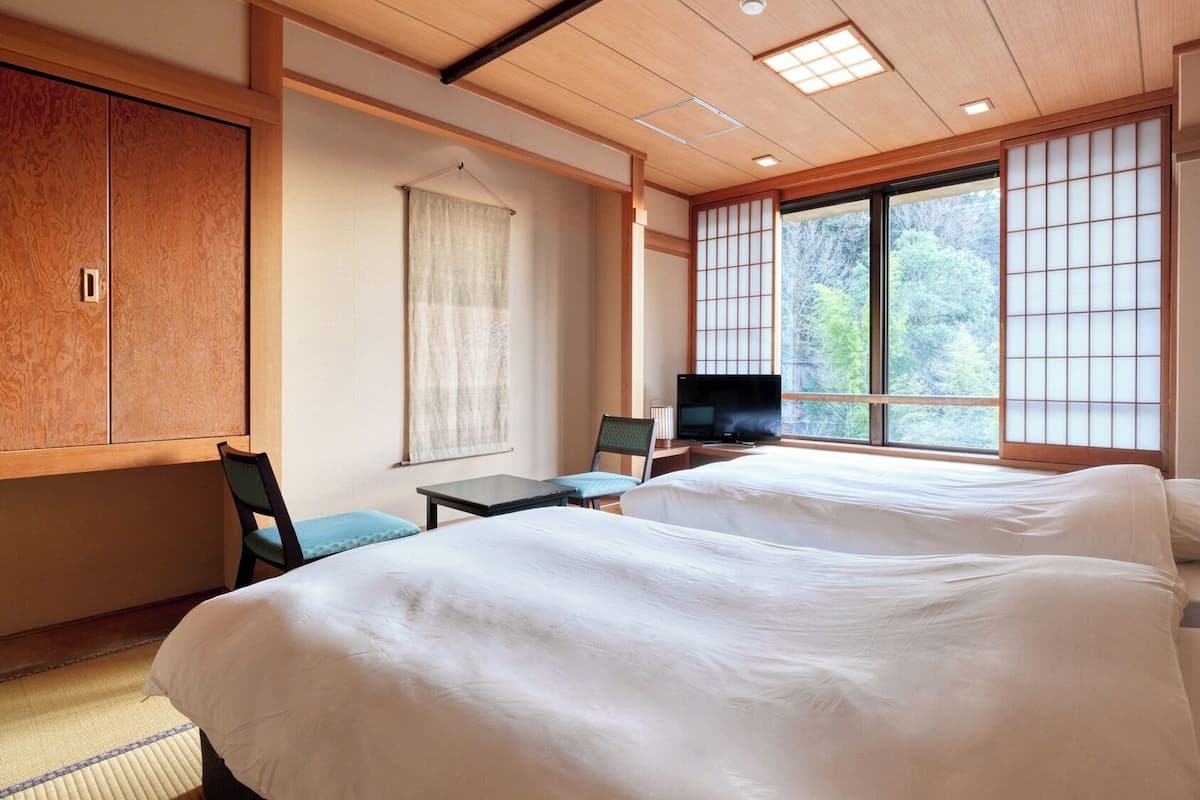 Une chambre d’hôtel avec un grand lit, une télévision, un bureau et une vue sur les arbres par la fenêtre.