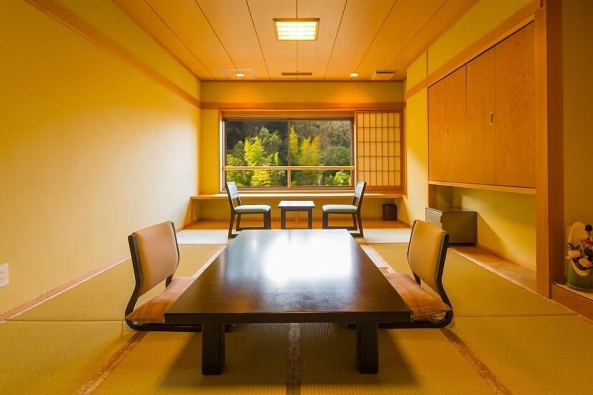 Une salle de conférence dotée d’une grande table, de quatre chaises, d’une vue sur les arbres par une fenêtre et de portes coulissantes traditionnelles japonaises.