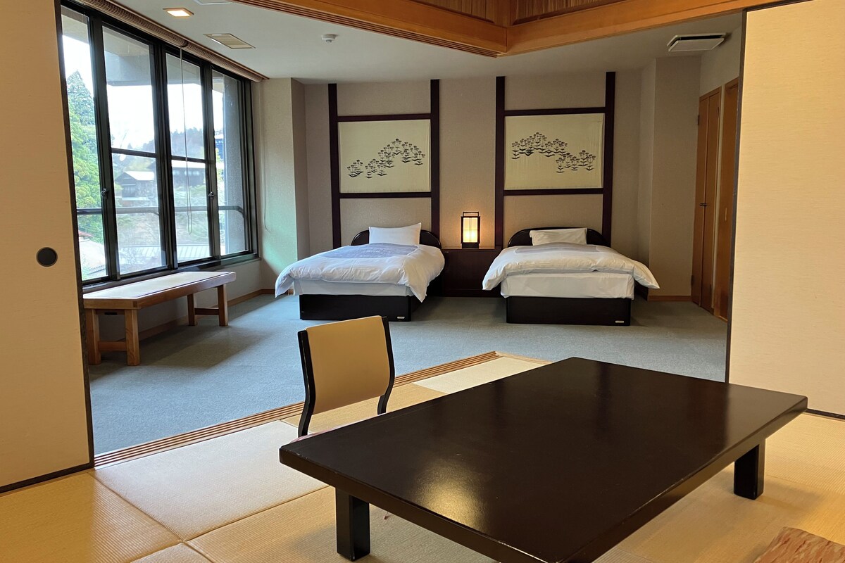 Habitación de hotel con dos camas, un banco de madera, una mesa, esteras de tatami y obras de arte en las paredes.