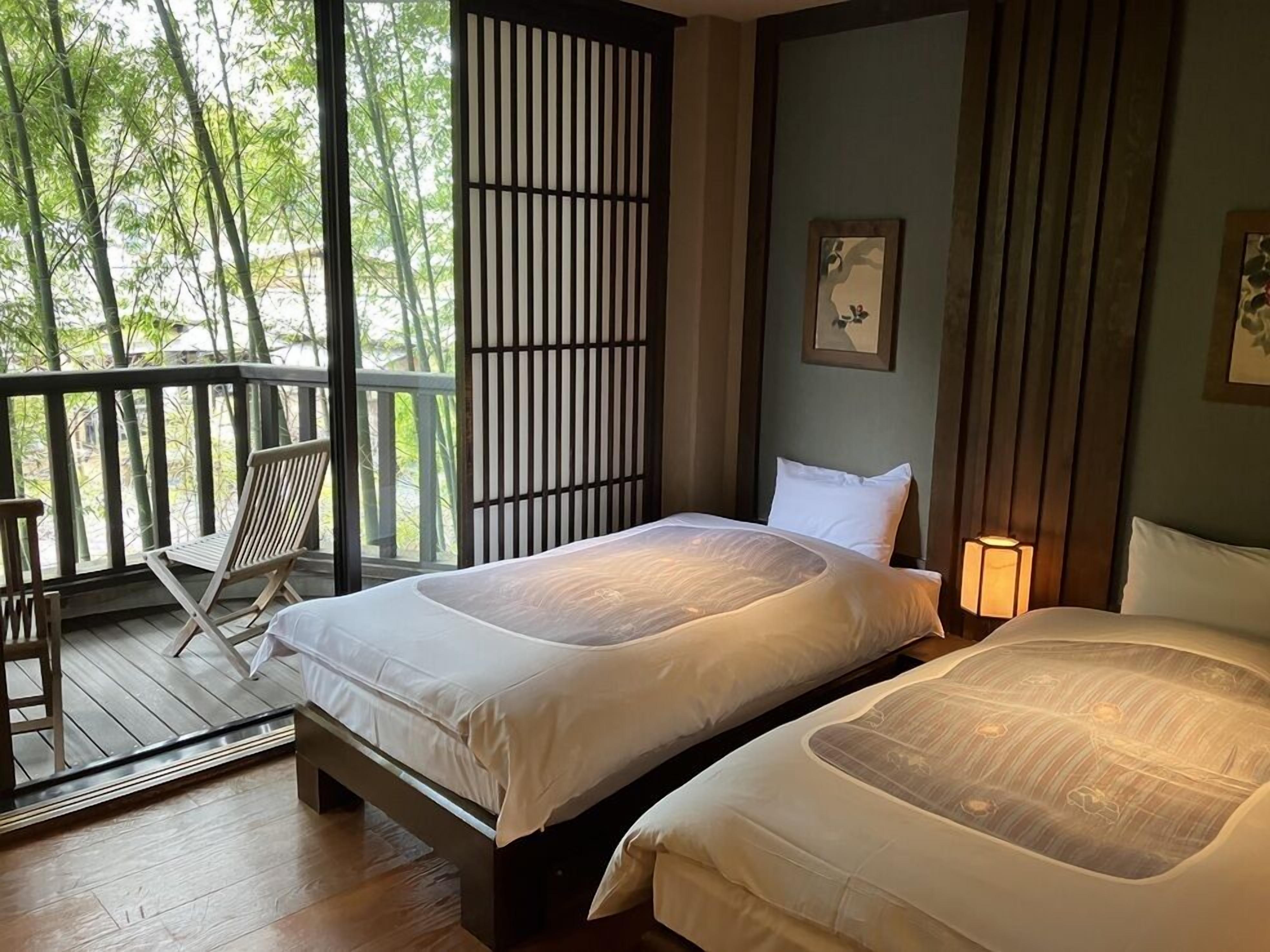 Een kamer met twee bedden, een houten terras en uitzicht op bomen.