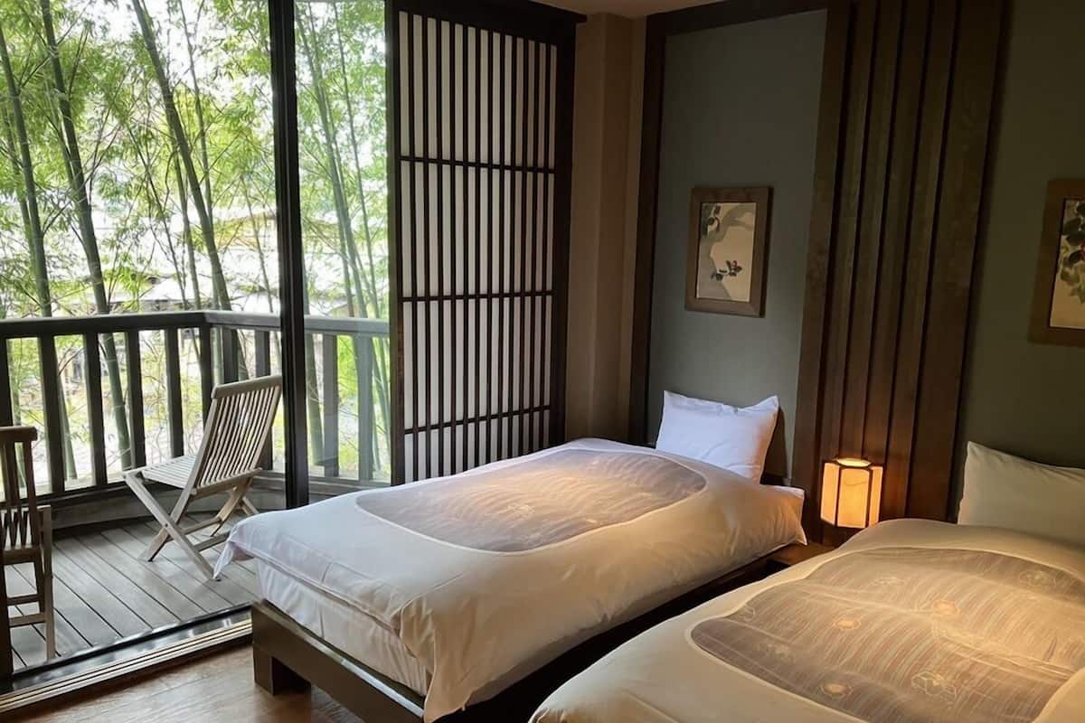 Une chambre avec deux lits, une terrasse en bois et une vue sur les arbres.