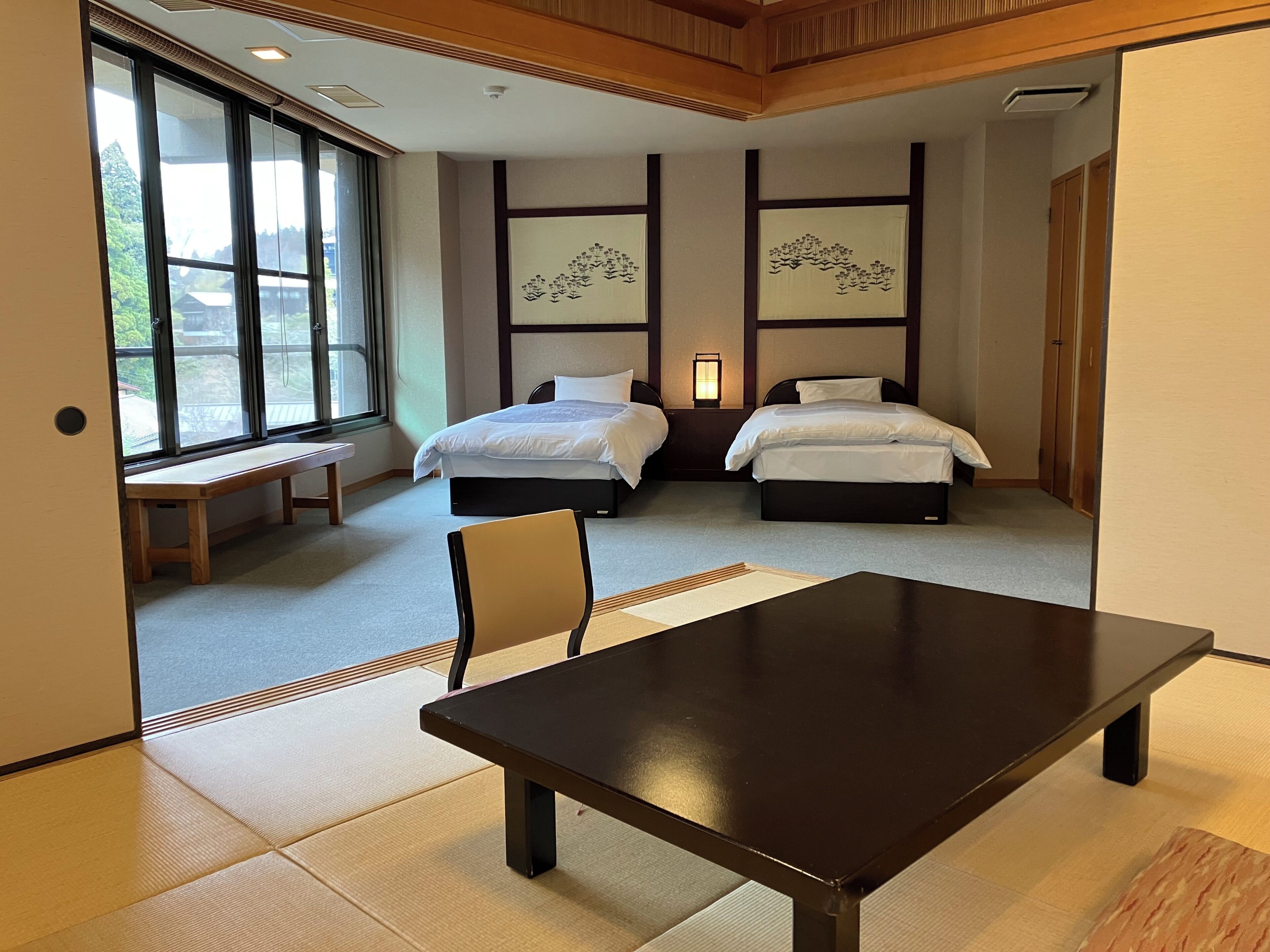 Een hotelkamer met twee bedden, een houten bankje, een tafel, tatami matten en kunstwerken aan de muren.