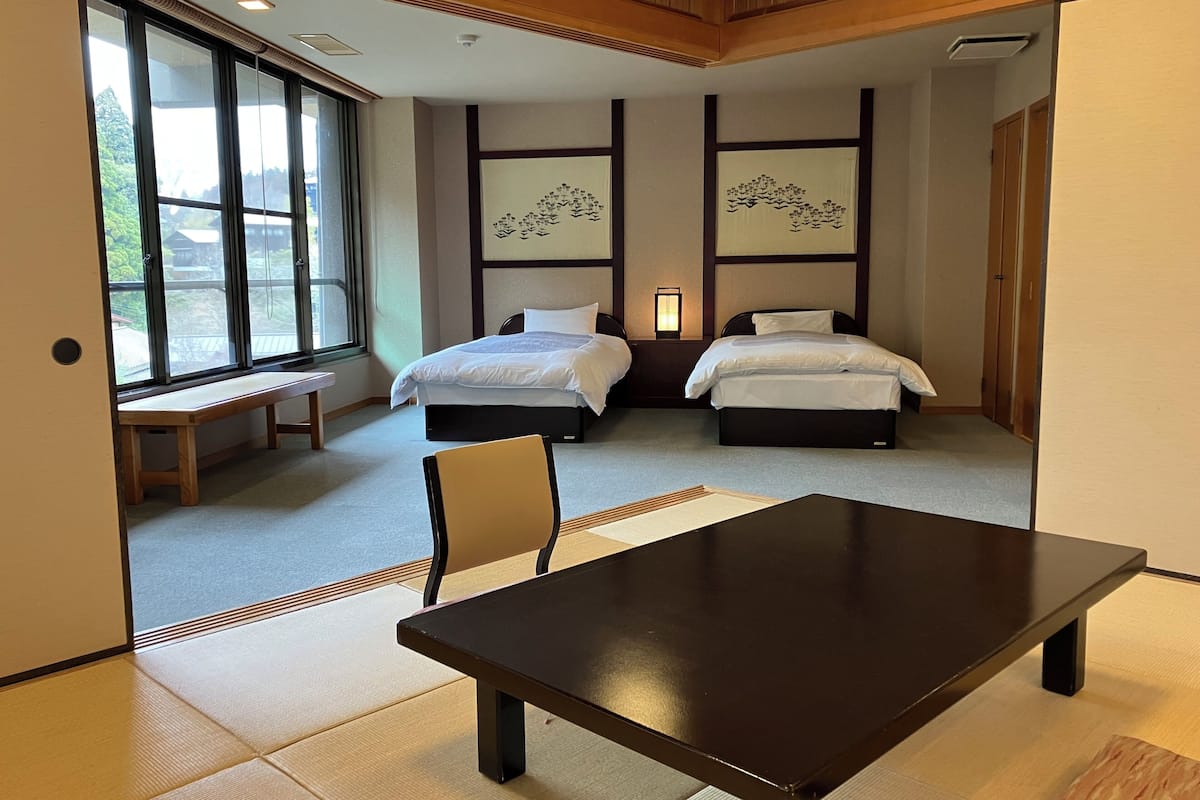 Une chambre d’hôtel avec deux lits, un banc en bois, une table, des tatamis et des œuvres d’art accrochées aux murs.
