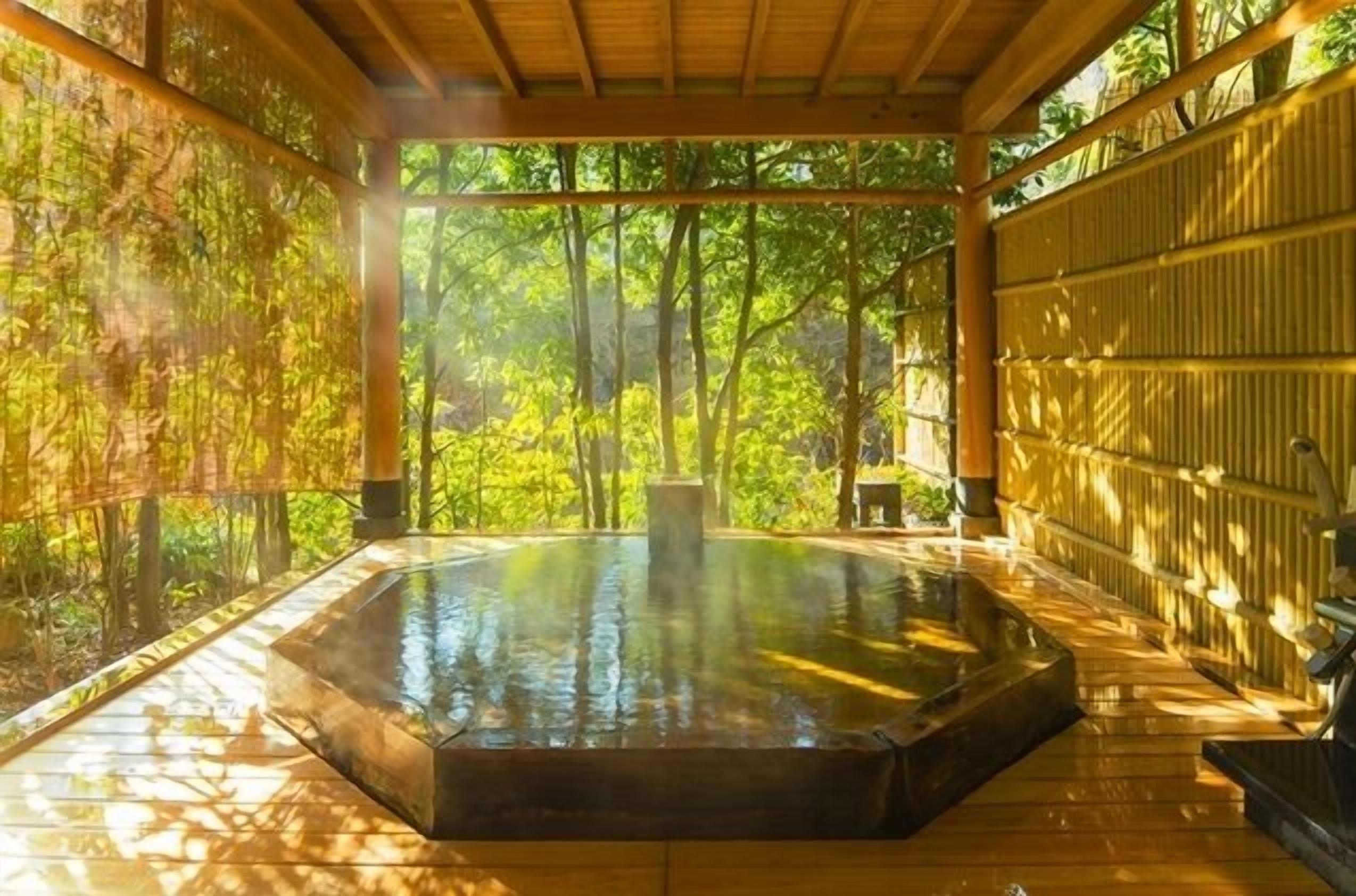 A hot spring bath area with a wooden deck, surrounded by bamboo walls and trees.