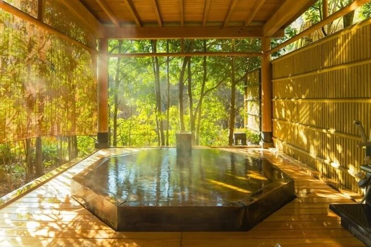 Un espace de baignade dans une source thermale, doté d’une terrasse en bois et entouré de murs et d’arbres en bambou.