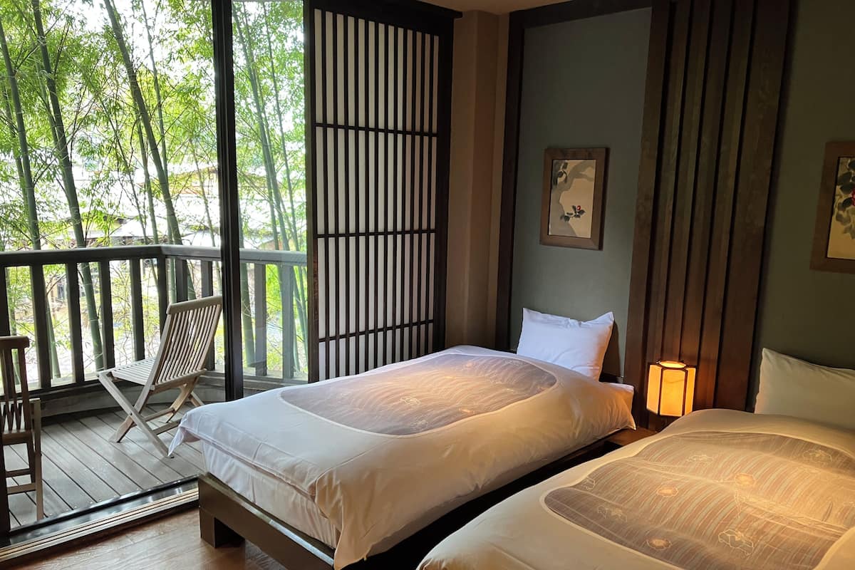 Une chambre avec deux lits, un balcon et une vue sur les arbres.
