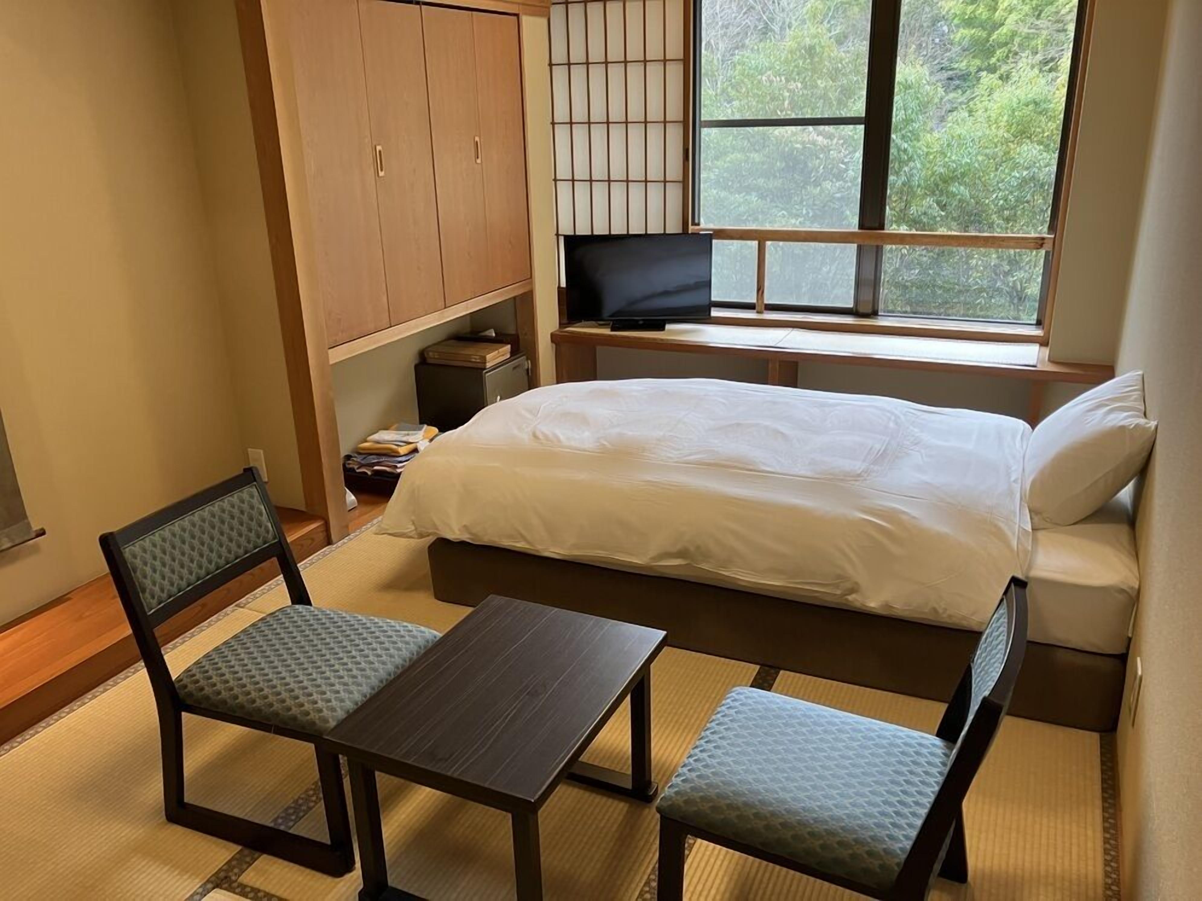 A bedroom with a bed, a TV, a desk, and two chairs.