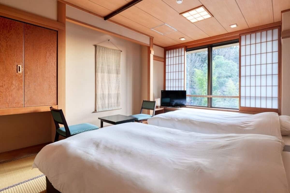 Une chambre d’hôtel équipée d’un lit, d’une télévision, d’un bureau et offrant une vue sur les arbres à travers de grandes fenêtres.