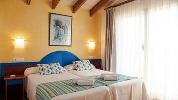 A hotel room with two beds, a wooden headboard, a painting on the wall, and a window with curtains.