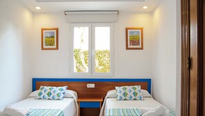 A double room with two beds, a wooden headboard, a window with blinds, and two framed pictures on the walls. - Sagitario Villas (Ciutadella de Menorca)