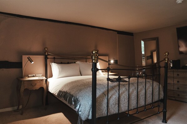 Un dormitorio con una cama con dosel, una mesita de noche con lámpara, un aparador y un espejo en la pared.