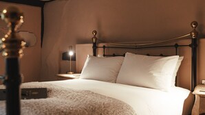 Een keurig opgemaakt bed met witte lakens, een donker metalen hoofdbord en een nachtkastje met een lamp.