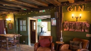 Een gezellig interieur van een pub met houten vloeren, leren fauteuils, een houten bar en een bord met de tekst 'GIN BEERS'.