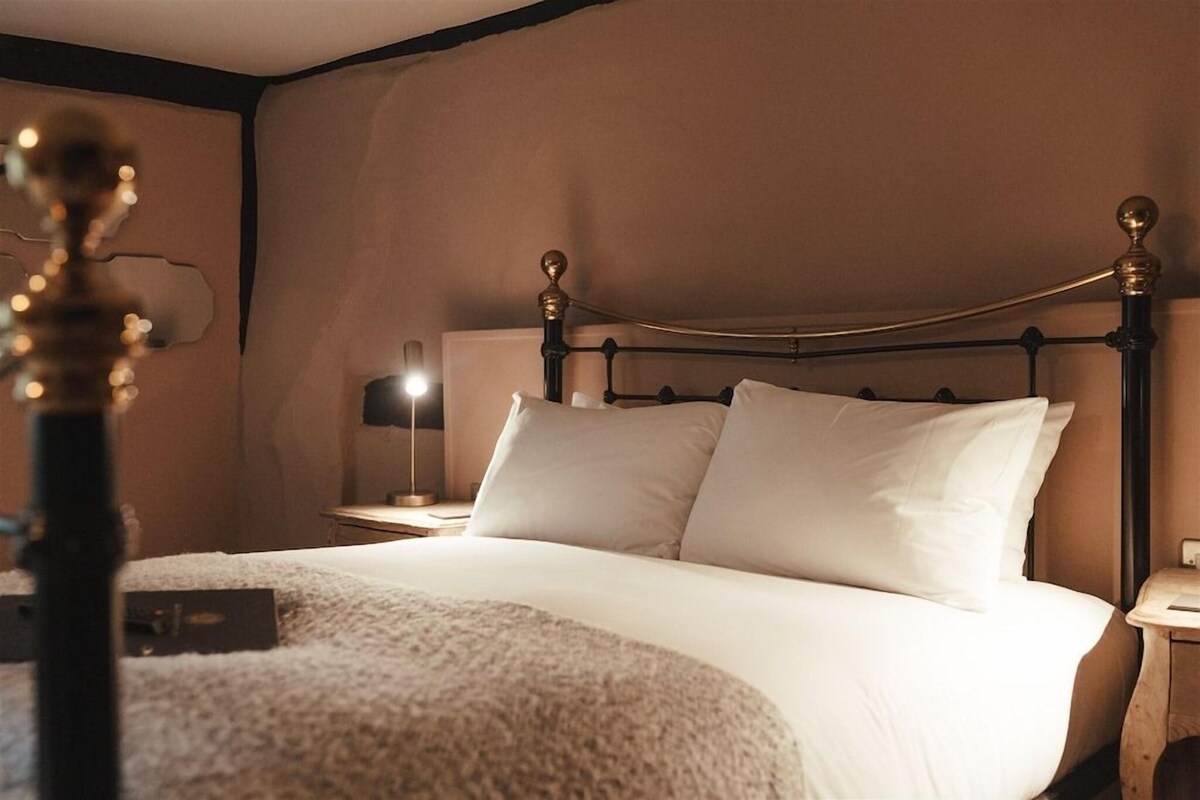 A neatly made bed with white linens, a dark metal headboard, and a bedside table with a lamp.