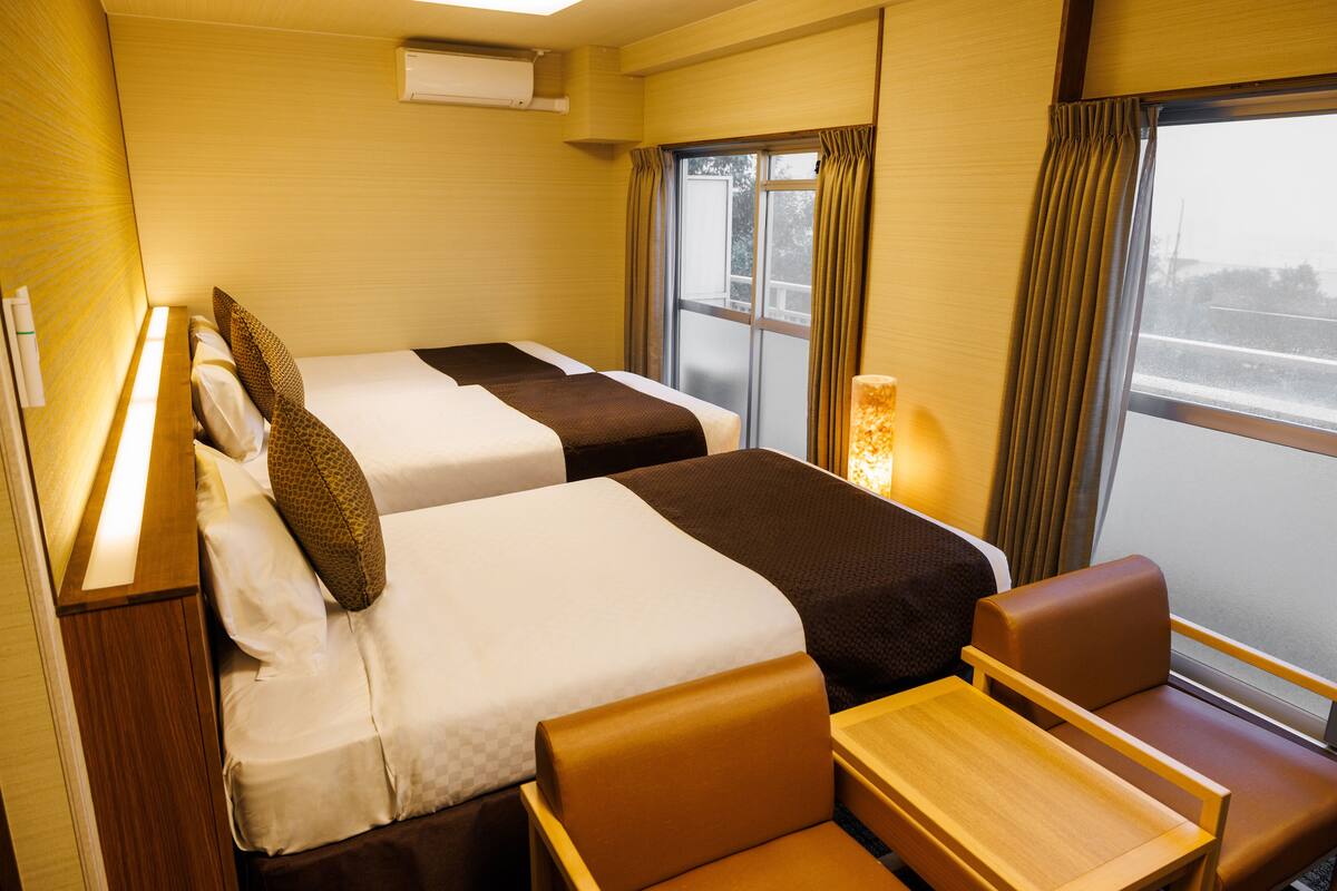 A hotel room with two beds, a small table, and a window with curtains.