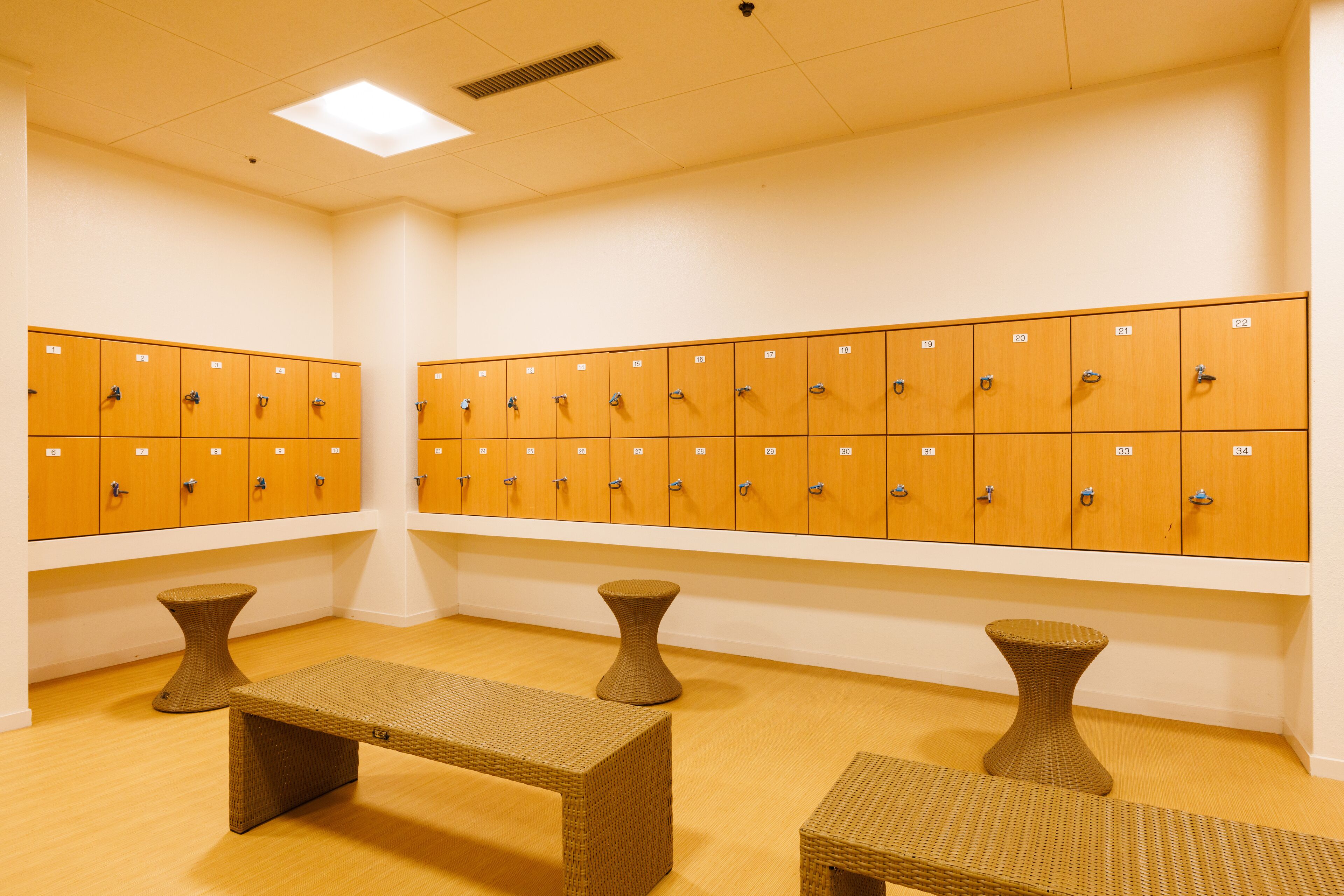 A locker room with multiple wooden lockers, a bench, and two stools.