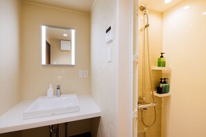 Een badkamer met een witte wasbak, spiegel en douche. Er staan toiletartikelen op de wasbak en een douchekop.