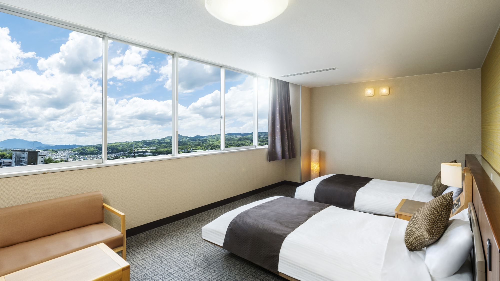 Ein Hotelzimmer mit zwei Betten, einem Schlafsofa, einem großen Fenster mit Blick auf Stadt und Berge sowie einer Deckenleuchte.