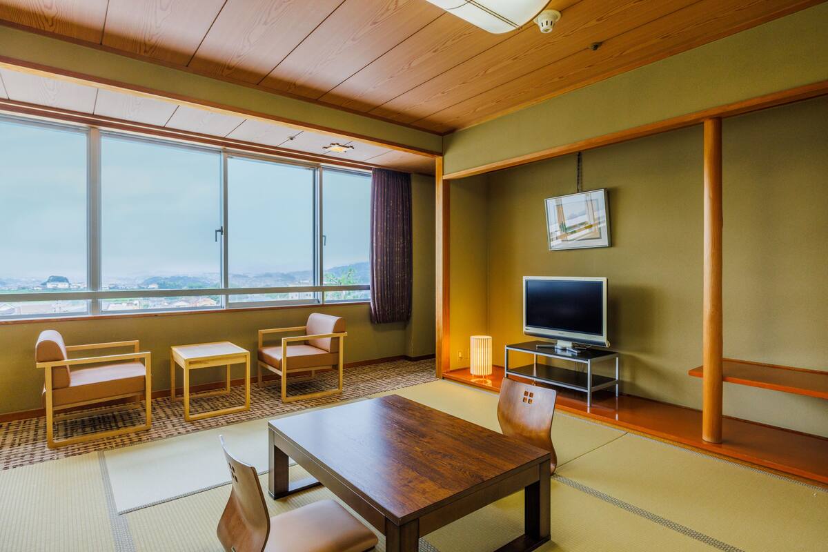 A room with a wooden ceiling, large windows, a television, a table, and two chairs.