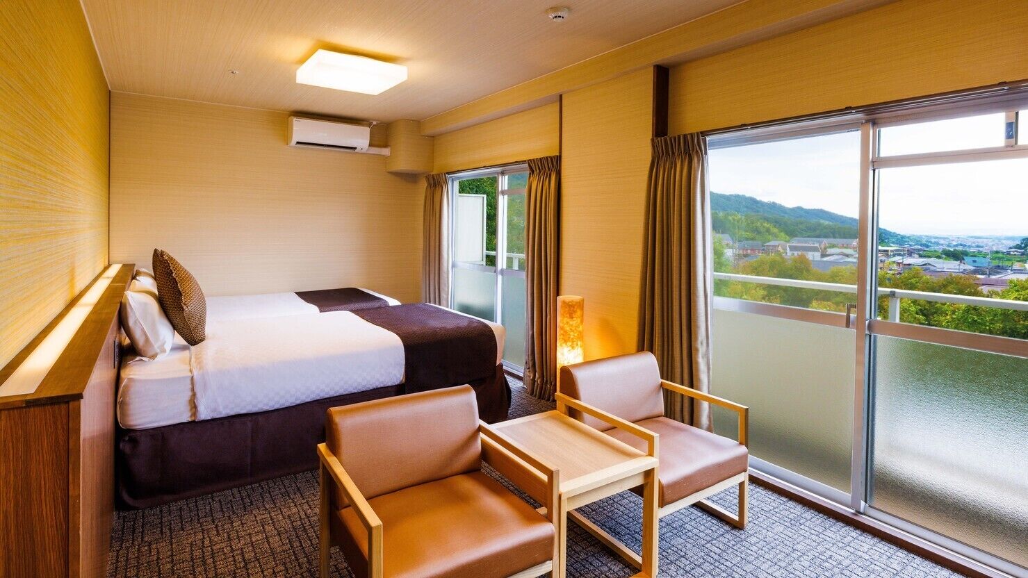 Ein Hotelzimmer mit Bett, zwei Sessel, einem kleinen Tisch, einem Fenster mit Blick und einer Klimaanlage.