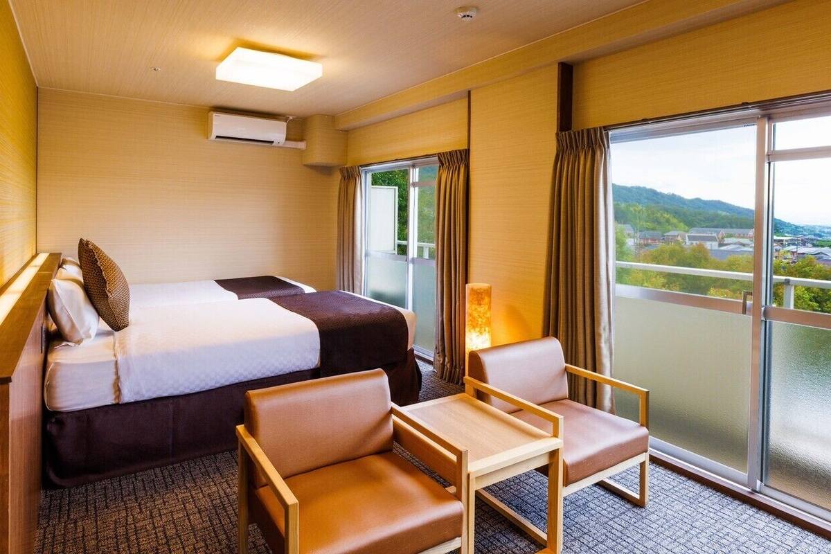 Ein Hotelzimmer mit Bett, zwei Sessel, einem kleinen Tisch, einem Fenster mit Blick und einer Klimaanlage.