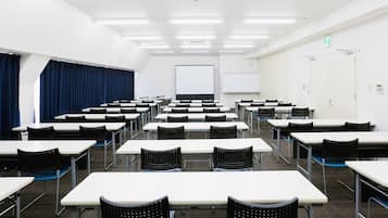 Sala de conferências com várias mesas e cadeiras, um quadro branco e uma tela de projeção.