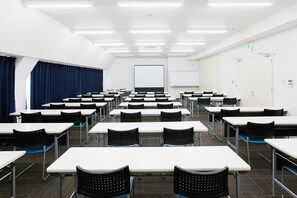 Une salle de conférence équipée de plusieurs tables et chaises, d’un tableau blanc et d’un écran de projection.