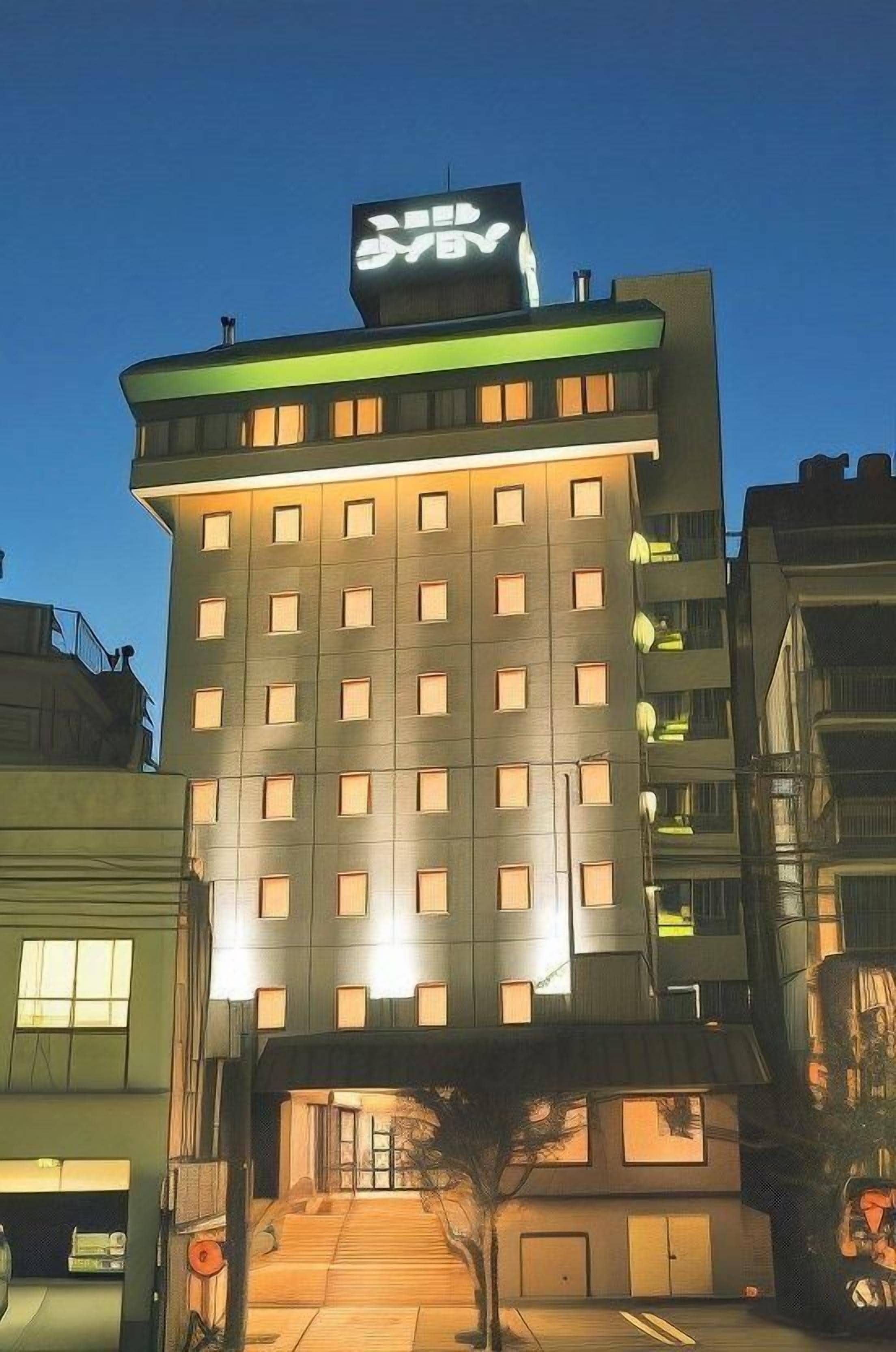A multi-story hotel with a prominent sign at the top, a well-lit entrance, and a visible parking area.