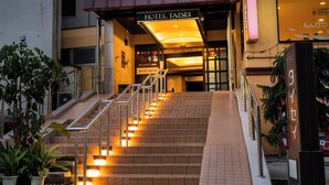 A hotel entrance with a staircase leading up to the lobby, a sign reading 'HOTEL TAISEI,' and a sign indicating the check-in hours. - Hotel Taisei (Kagoshima)