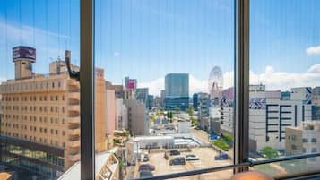 Vista urbana pela janela, com edifícios, um estacionamento e uma roda gigante ao longe.