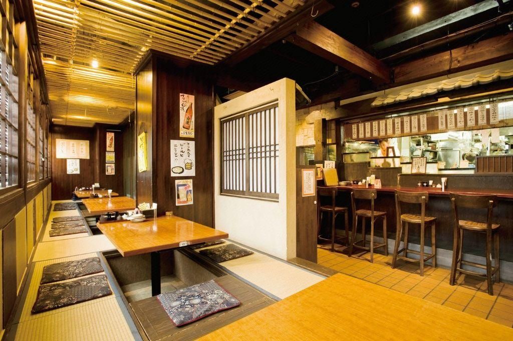 A traditional Japanese restaurant interior with tatami mats, wooden tables, and a counter with stools.