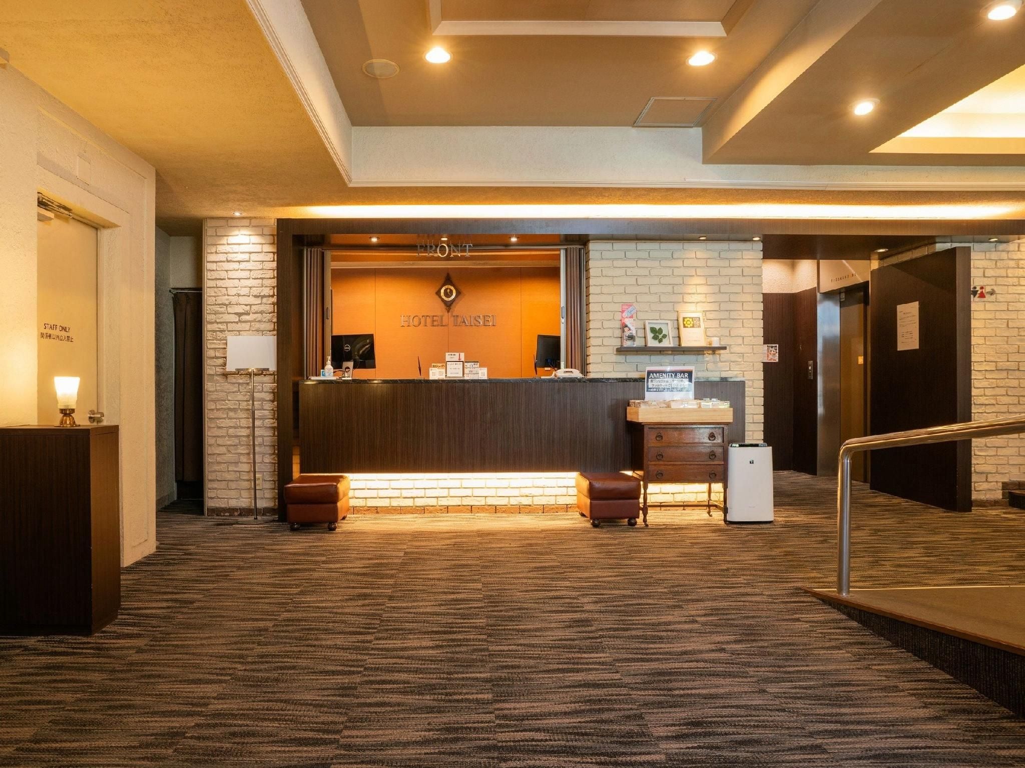 A hotel reception area with a wooden reception desk, a sign reading 'HOTEL TAISEI,' and a 'STAFF ONLY' sign on the wall.