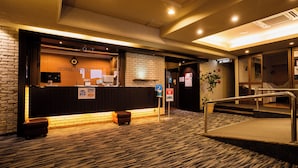 A hotel reception area with a reception desk, a sign for the toilet, a plant, and a staircase leading to another floor. - Hotel Taisei (Kagoshima)